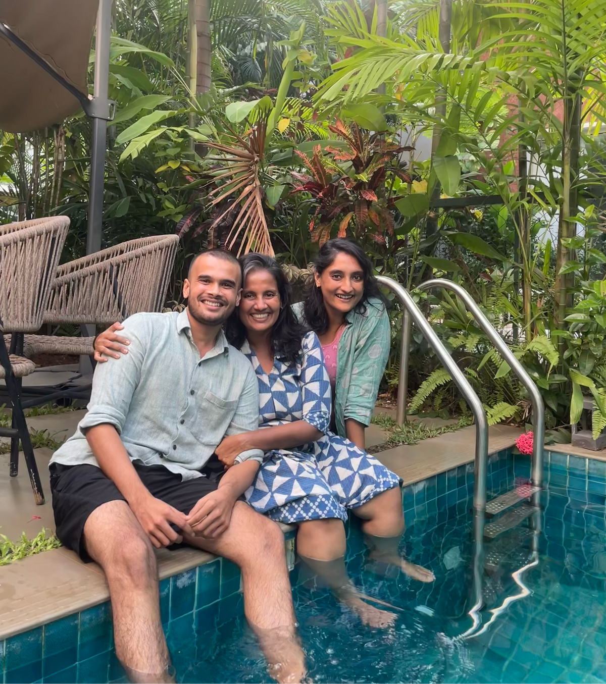Three people sitting by a pool with lush greenery in the background