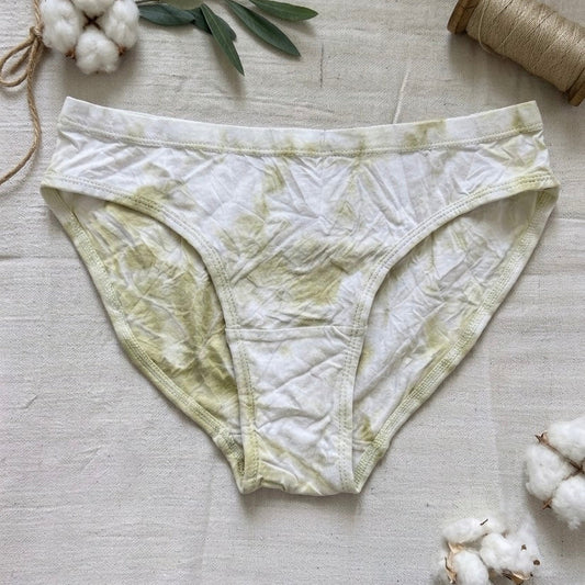 Green and white patterned underwear on a light wooden surface with cotton and twine.