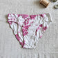 Pink and white tie-dye underwear on a textured surface with a wooden spool and green leaves.