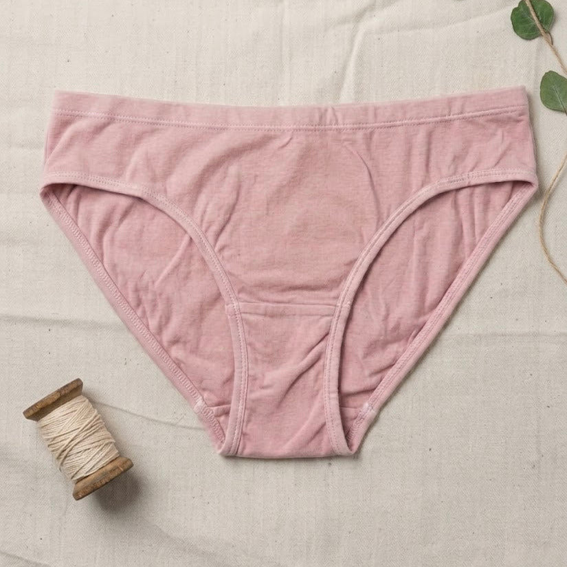 Pink underwear on a textured surface with a spool of thread and green leaves.