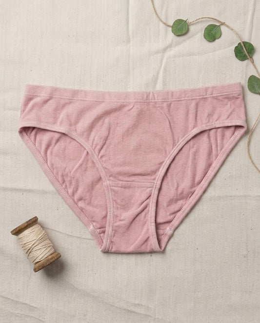 Pink underwear on a textured surface with a spool of thread and green leaves.